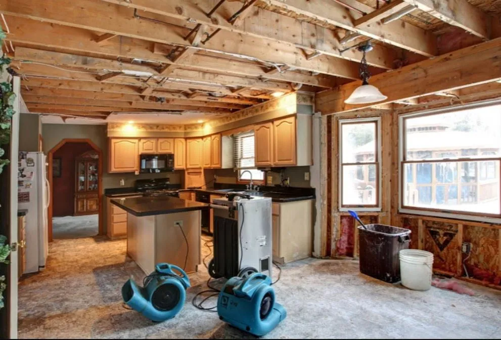 Water-damaged kitchen with exposed wooden framing and industrial drying equipment