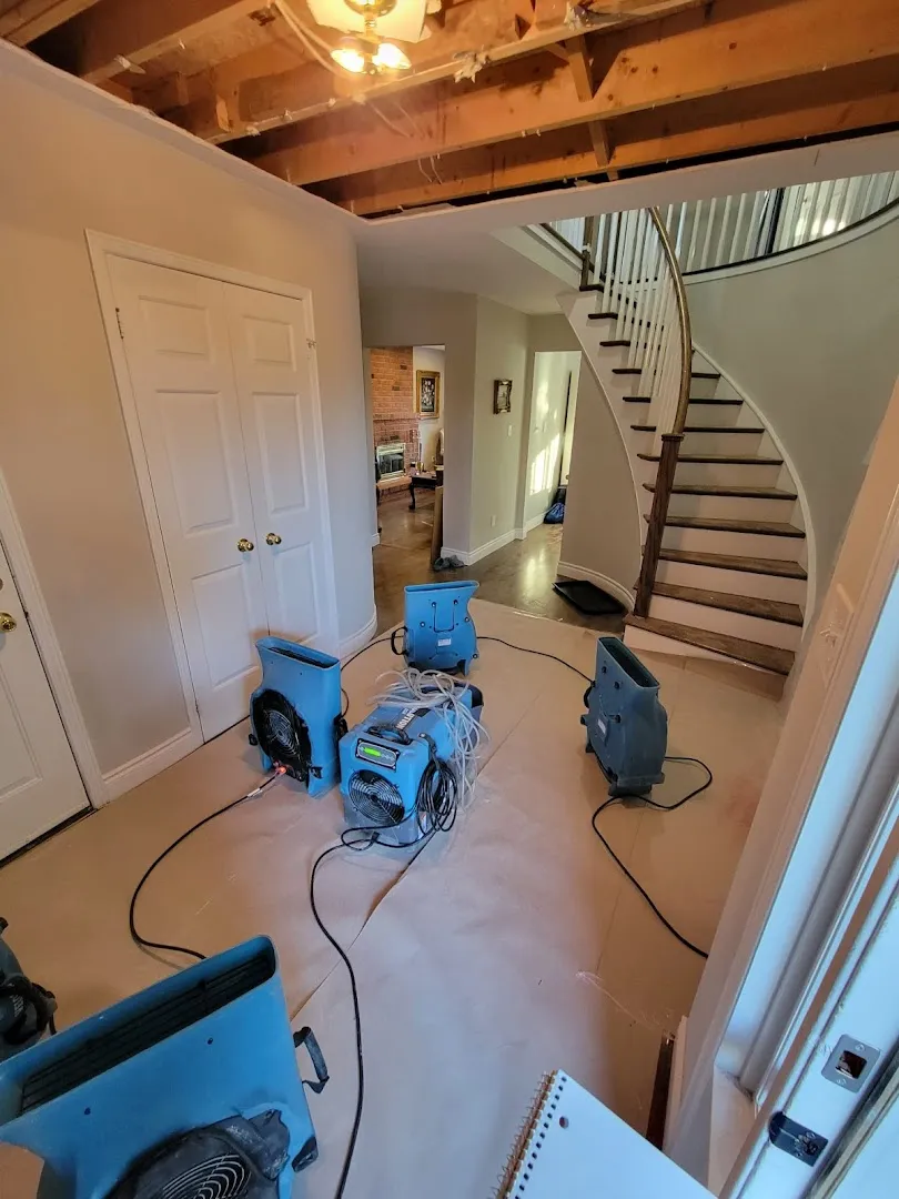 Hallway with exposed ceiling damage and multiple blue industrial dehumidifiers drying water-damaged home