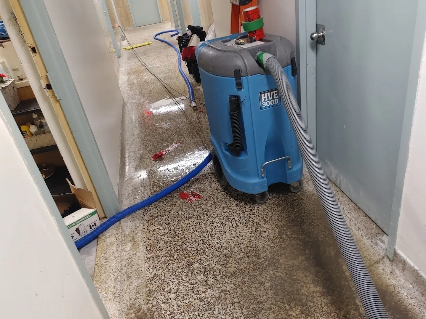 Blue water extraction equipment deployed on wet flooring during carpet drying process