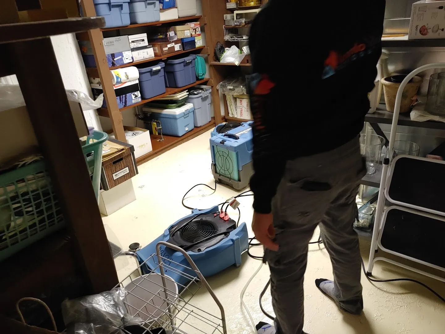 Restoration technician operating dehumidifier and water removal equipment in finished basement space