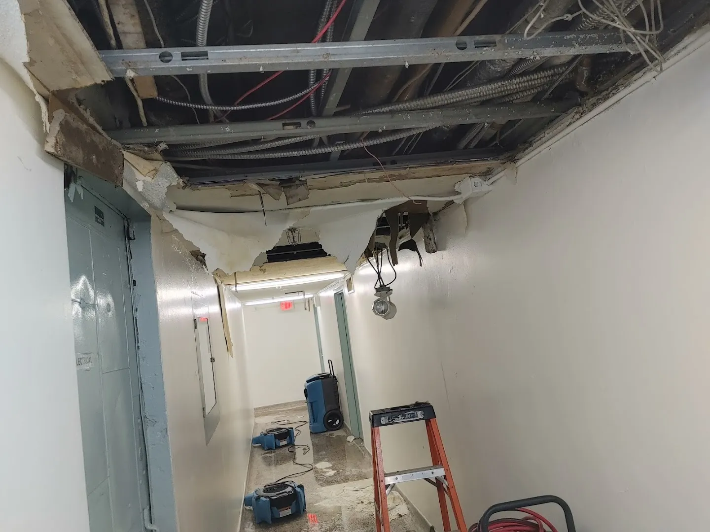 Damaged ceiling with exposed wiring, metal framework and drying equipment in utility corridor