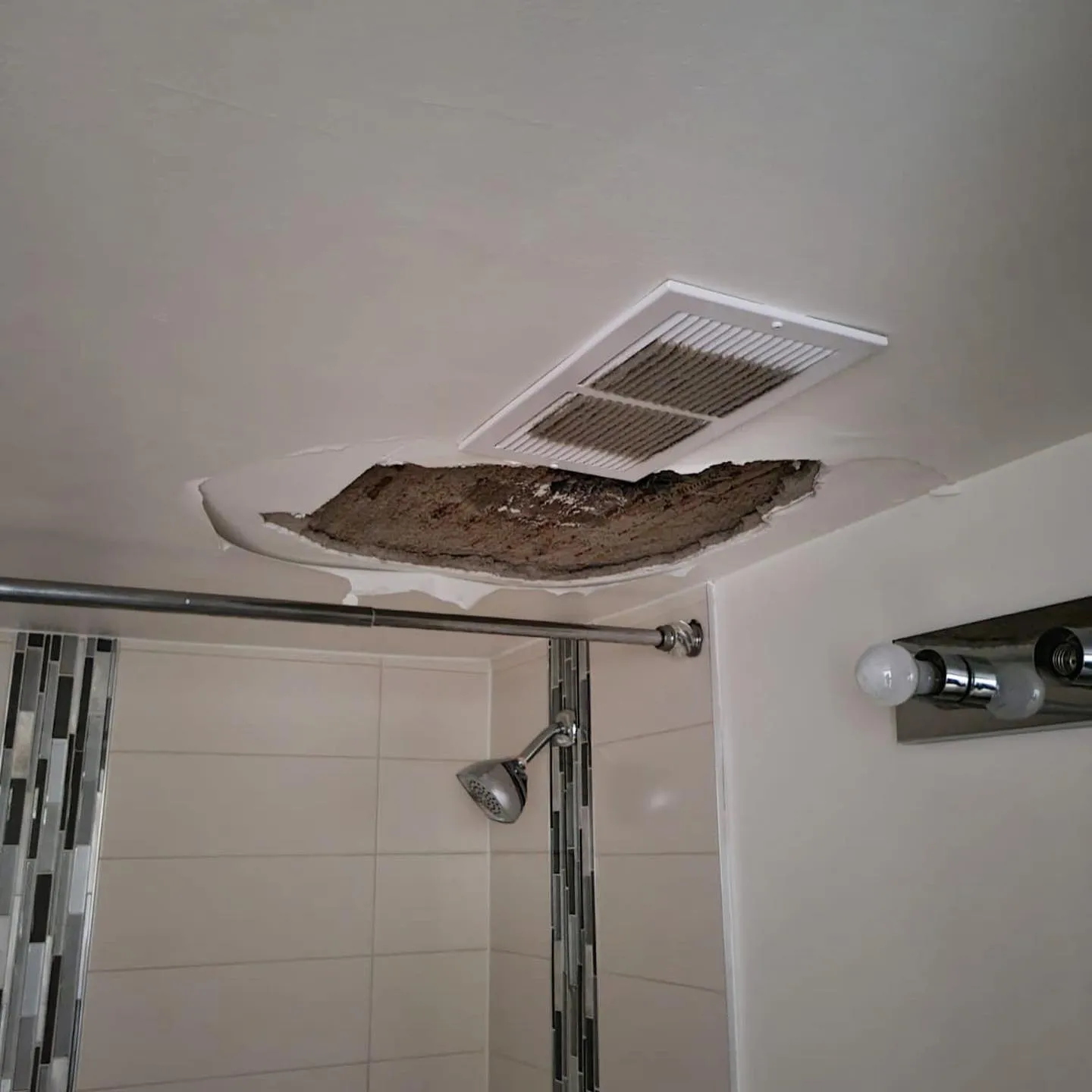 Water-damaged bathroom ceiling with torn drywall and exposed cavity above shower enclosure