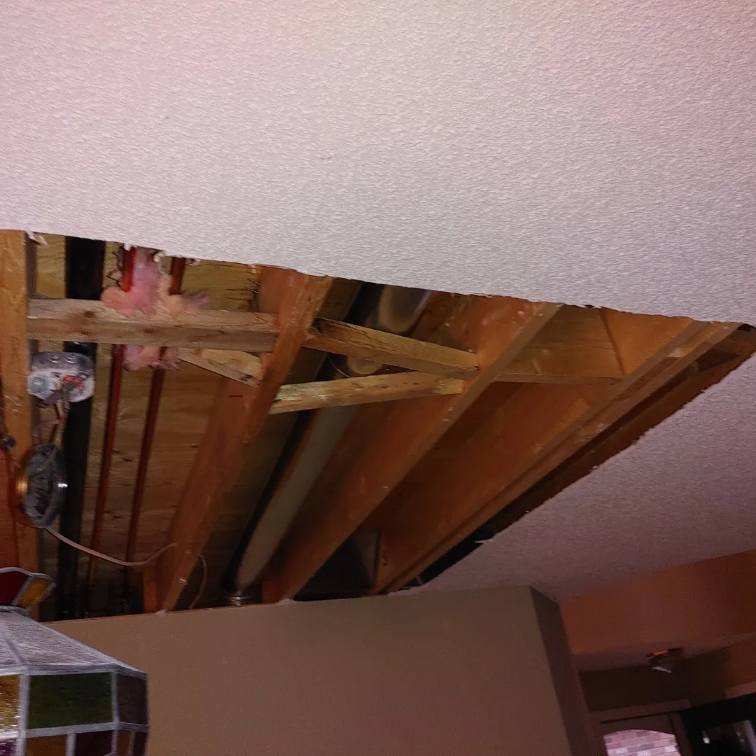 Severely water-damaged ceiling showing exposed wooden joists, wet insulation, and structural damage from water intrusion